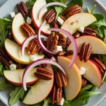 Delicious Apple Arugula Salad topped with Maple Pecans on a wooden table