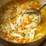 Bowl of easy lemon chicken orzo soup with fresh herbs and lemon slices