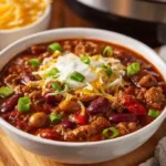 Bowl of homemade classic chili with garnishes and ingredients on the side